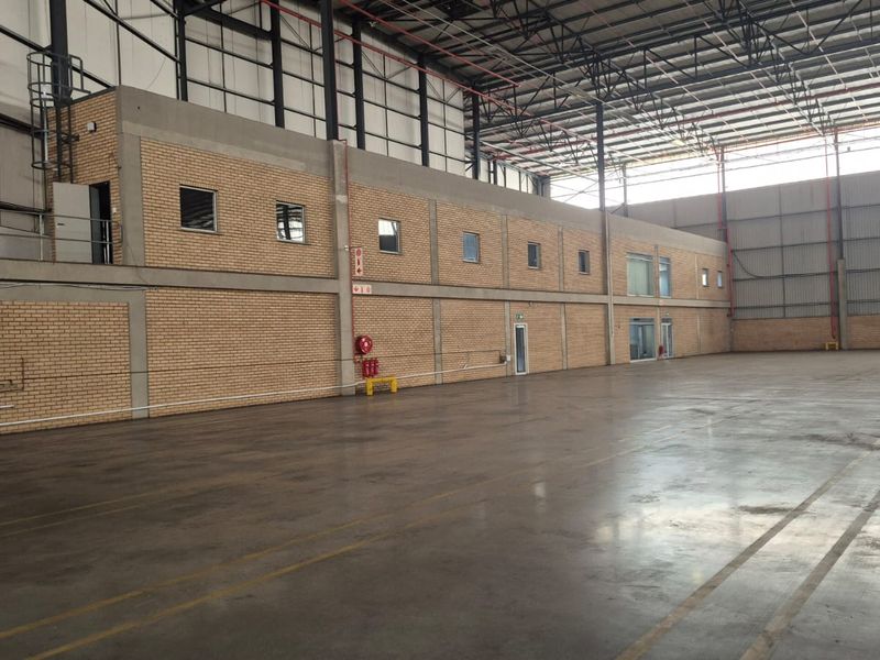Spacious industrial warehouse featuring high ceilings with exposed steel trusses, polished concrete flooring, and a functional mezzanine level with integrated office or storage space.
