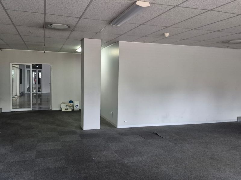 A spacious, open-plan industrial office area featuring a suspended ceiling, carpeted flooring, and a central structural column, offering a versatile workspace layout.