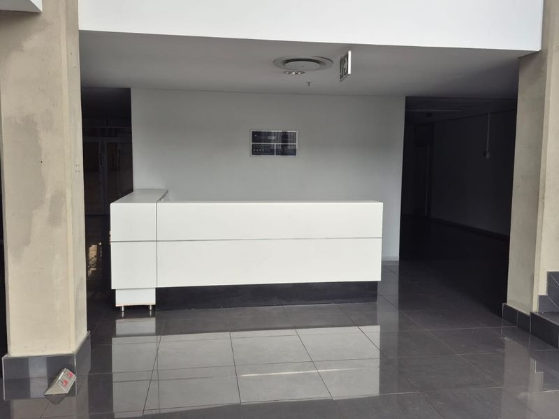 Modern industrial entrance lobby featuring a built-in reception desk, polished dark floor tiles, and concrete structural columns.
