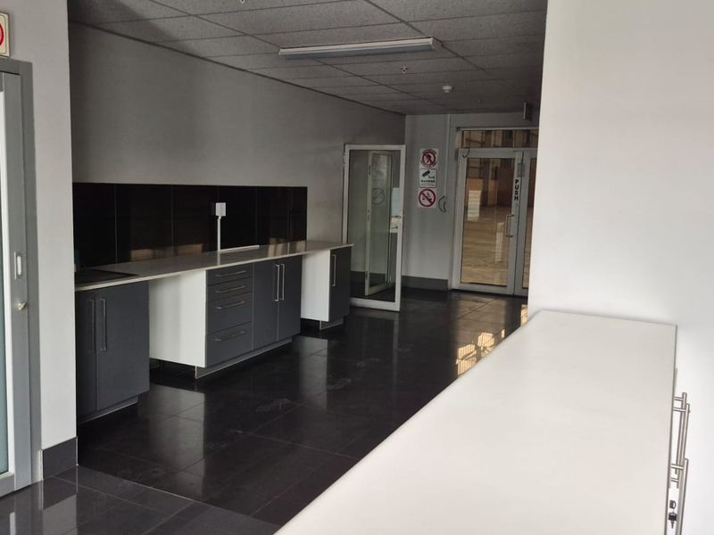 A clean, modern industrial kitchenette featuring dark cabinetry, contrasting countertops, tiled flooring, and a drop ceiling with integrated lighting.