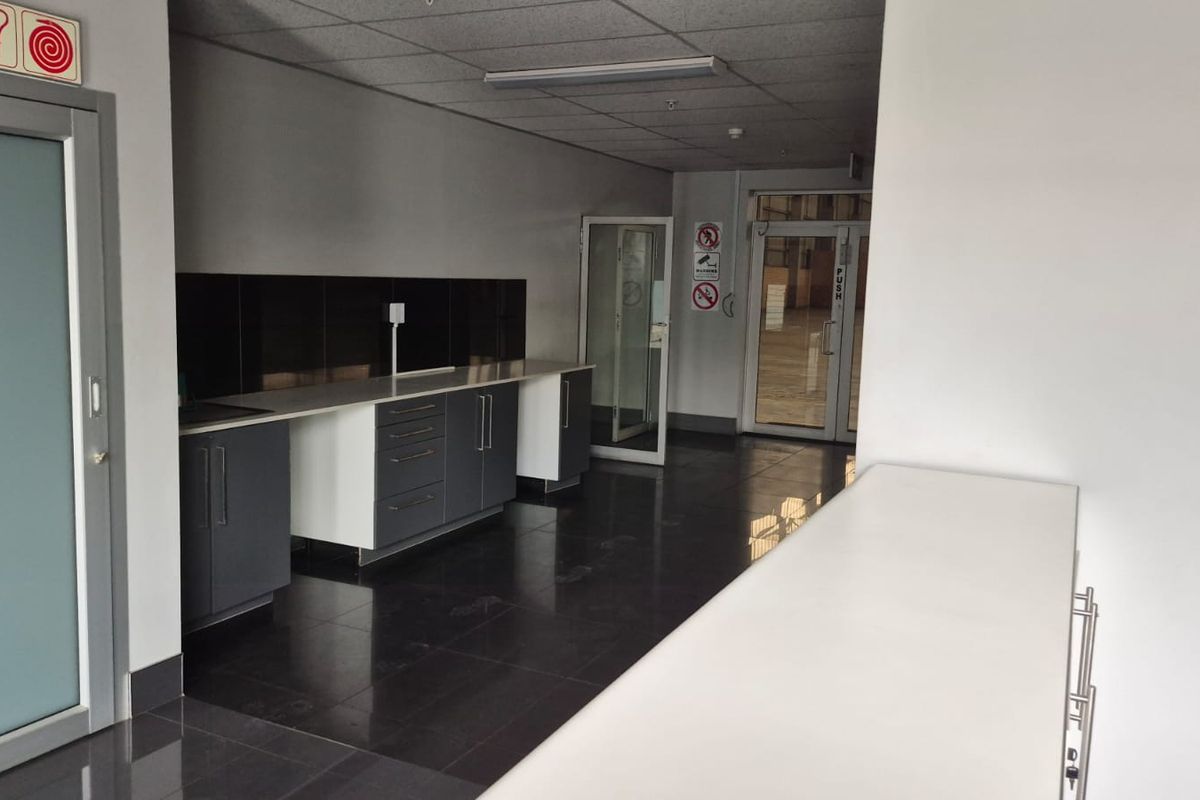 A clean, modern industrial kitchenette featuring dark cabinetry, contrasting countertops, tiled flooring, and a drop ceiling with integrated lighting.