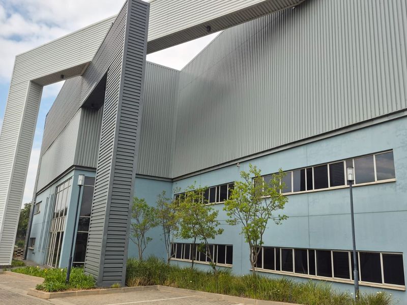 Modern industrial building facade featuring corrugated metal cladding, architectural steel framing, and extensive aluminium-framed windows with paved parking access.