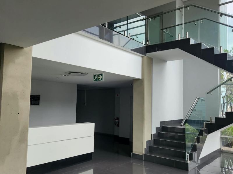 Modern industrial office entrance featuring a sleek reception desk, tiled flooring, and a contemporary staircase with glass balustrades.