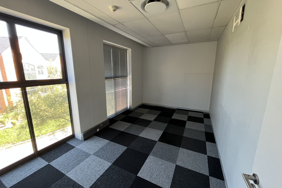 A vacant office space featuring a suspended ceiling, carpet tile flooring, and large windows with venetian blinds, offering a clean and functional workspace.