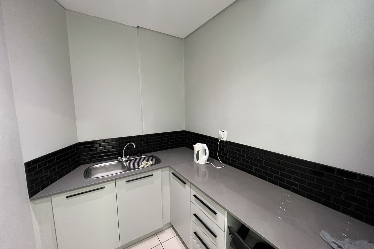 A compact, modern kitchenette featuring stone countertops, a stainless steel sink, and a stylish black subway tile backsplash with ample built-in storage.