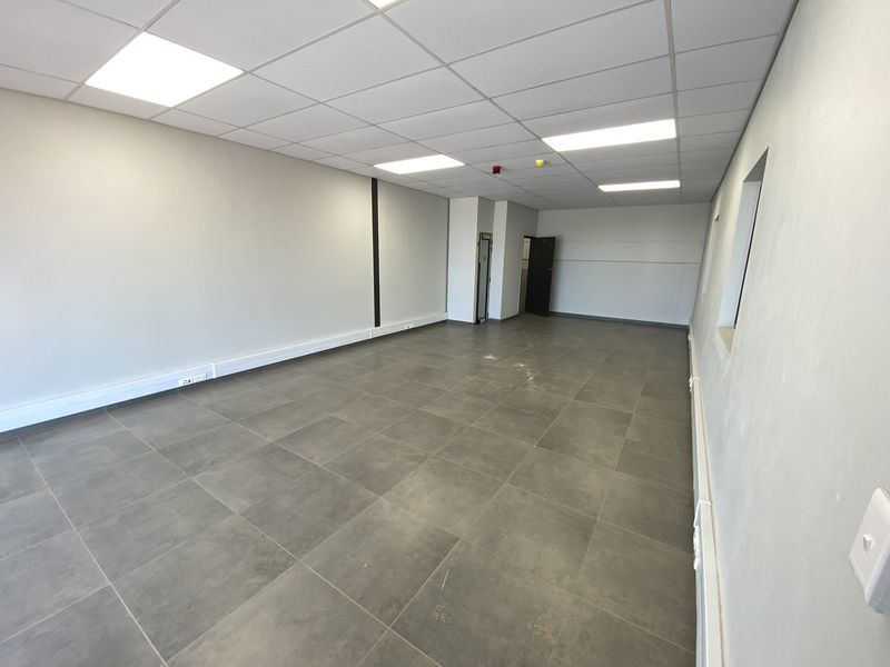 A clean, vacant industrial office space featuring modern grey tiled flooring, a suspended ceiling with recessed lighting, and perimeter electrical trunking.