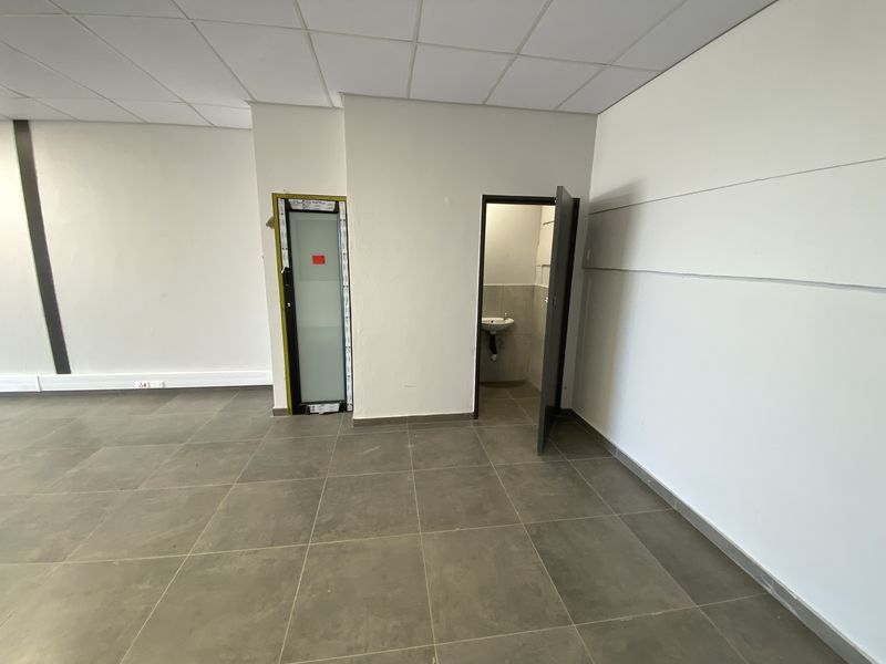 An open-plan industrial office space featuring tiled flooring, a suspended ceiling, and a private internal washroom with a wall-mounted basin.