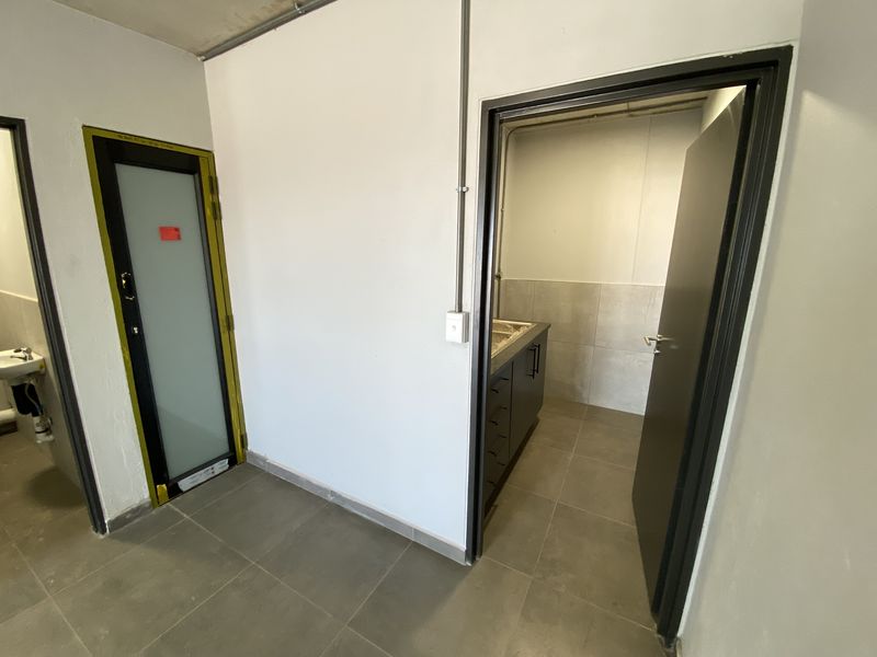A functional hallway area featuring tiled flooring, exposed conduit, and access to adjacent utility spaces with modern door frames.