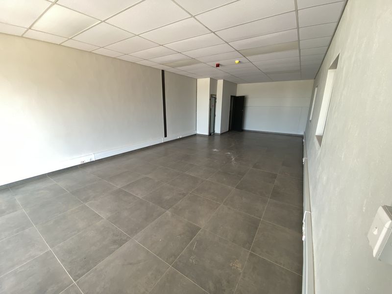 An empty, open-plan industrial office space featuring tiled flooring, a suspended ceiling, and surface-mounted electrical trunking.