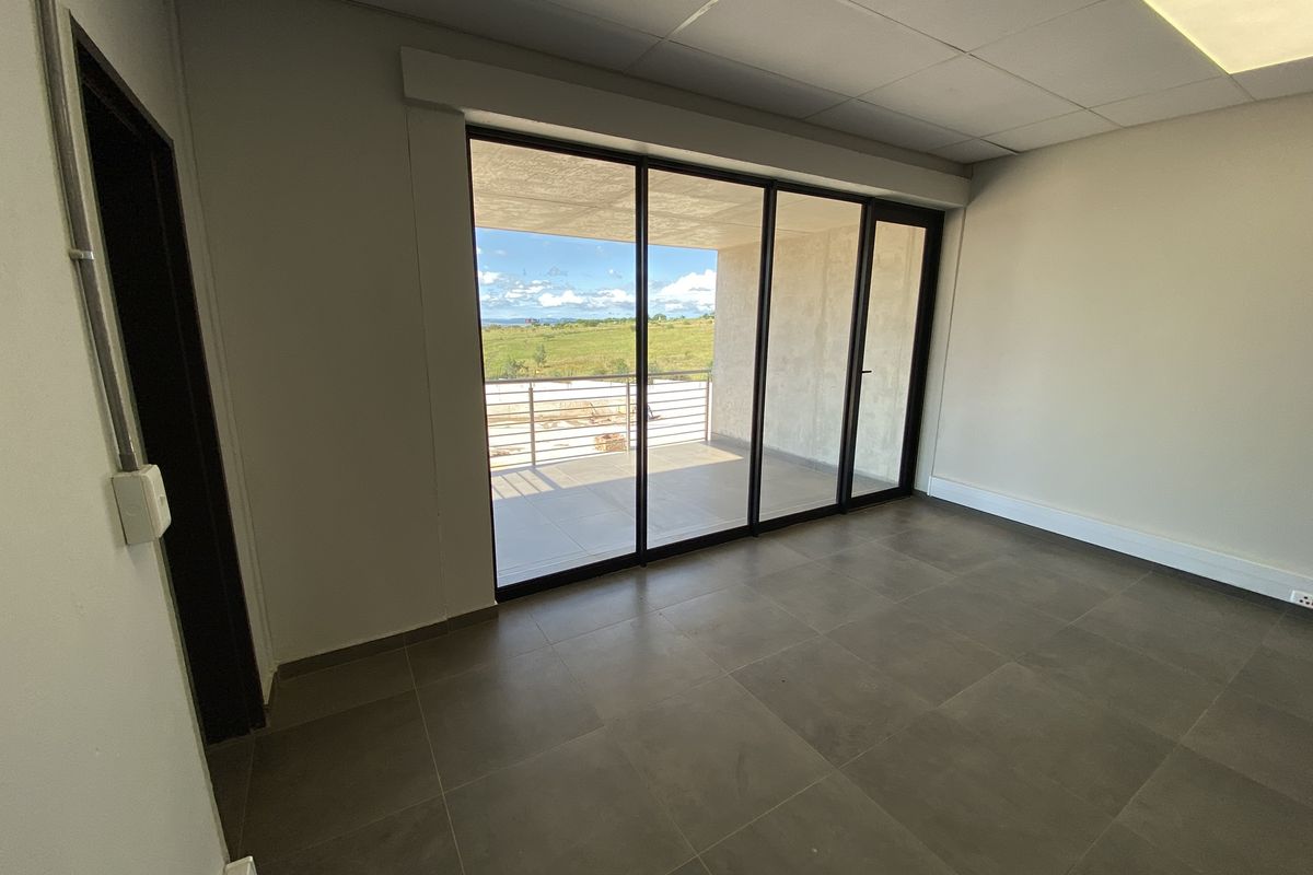 A bright, modern office space featuring large sliding glass doors that open onto a private balcony with scenic views.