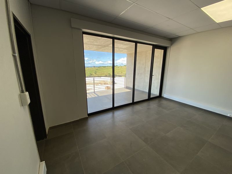 A bright, modern office space featuring large sliding glass doors that open onto a private balcony with scenic views.