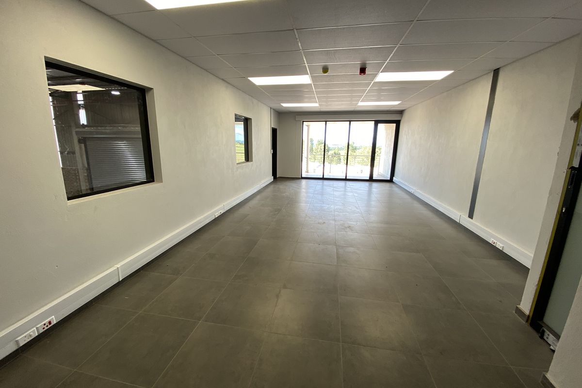 A spacious, modern office area featuring tiled flooring, a suspended ceiling with recessed lighting, and large sliding glass doors leading to an outdoor space.