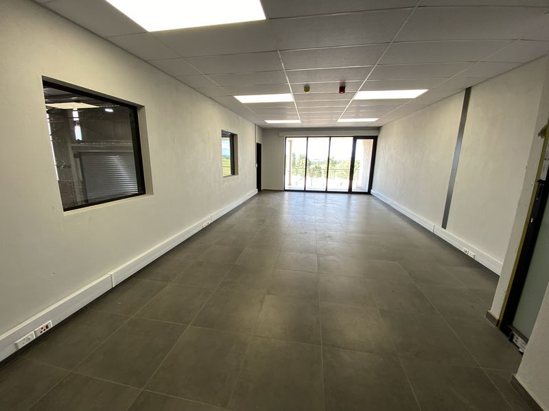 A spacious, modern office area featuring tiled flooring, a suspended ceiling with recessed lighting, and large sliding glass doors leading to an outdoor space.