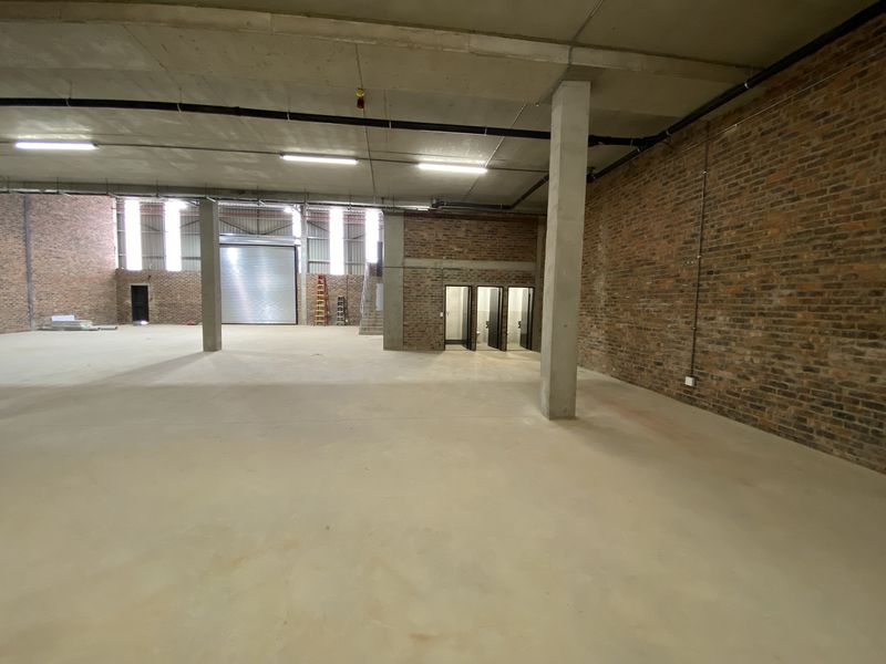 Spacious industrial warehouse unit featuring exposed brick walls, concrete flooring, high ceilings, and a large roller shutter door for easy access.