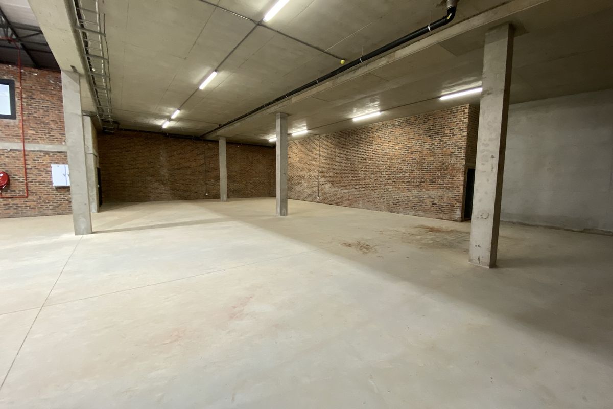 Spacious industrial utility area featuring exposed brick walls, concrete flooring, and high ceilings with functional overhead lighting.