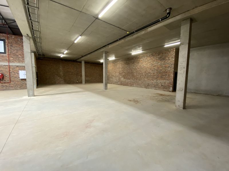 Spacious industrial utility area featuring exposed brick walls, concrete flooring, and high ceilings with functional overhead lighting.