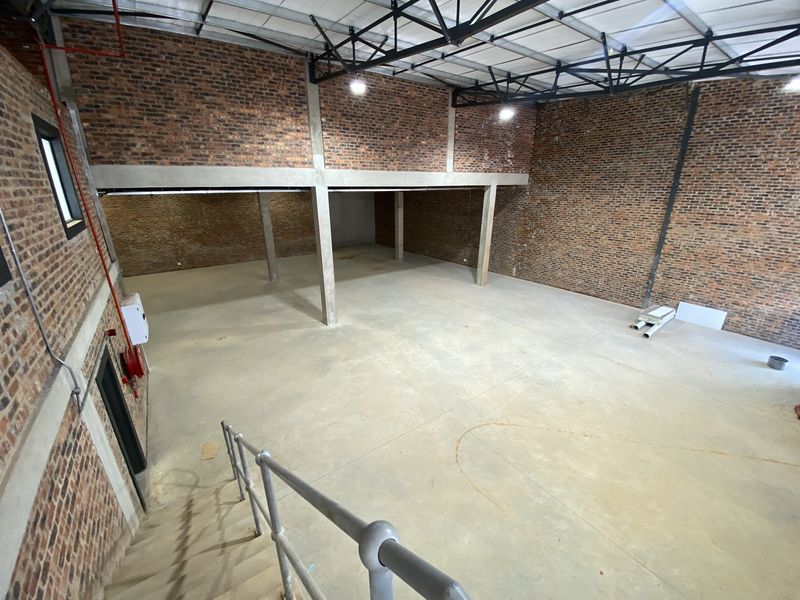 Spacious industrial open-plan warehouse area featuring exposed brick walls, concrete flooring, and high-clearance steel roof trusses, suitable for various commercial or creative uses.