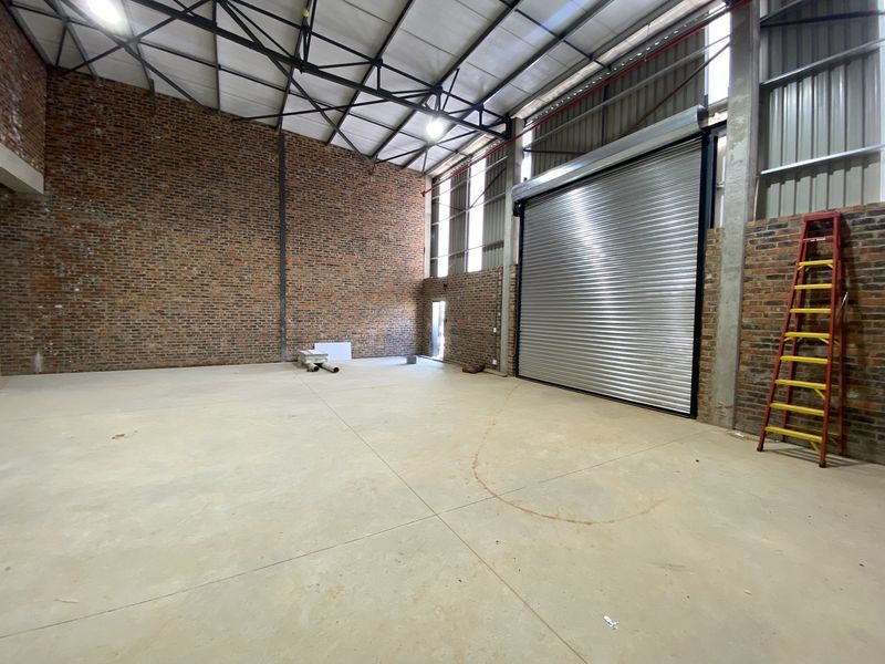 Spacious industrial warehouse unit featuring high ceilings, exposed brick walls, concrete flooring, and a large roller shutter door for easy access.