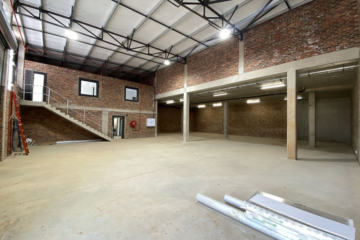 Spacious industrial warehouse unit featuring exposed brick walls, high ceilings with steel trusses, concrete flooring, and an internal staircase.