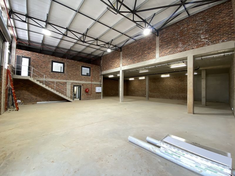 Spacious industrial warehouse unit featuring exposed brick walls, high ceilings with steel trusses, concrete flooring, and an internal staircase.
