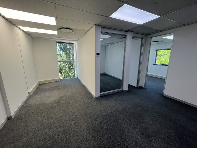 An empty office space featuring glass partitions, carpeted flooring, and recessed lighting, offering a clean and functional layout for professional use.