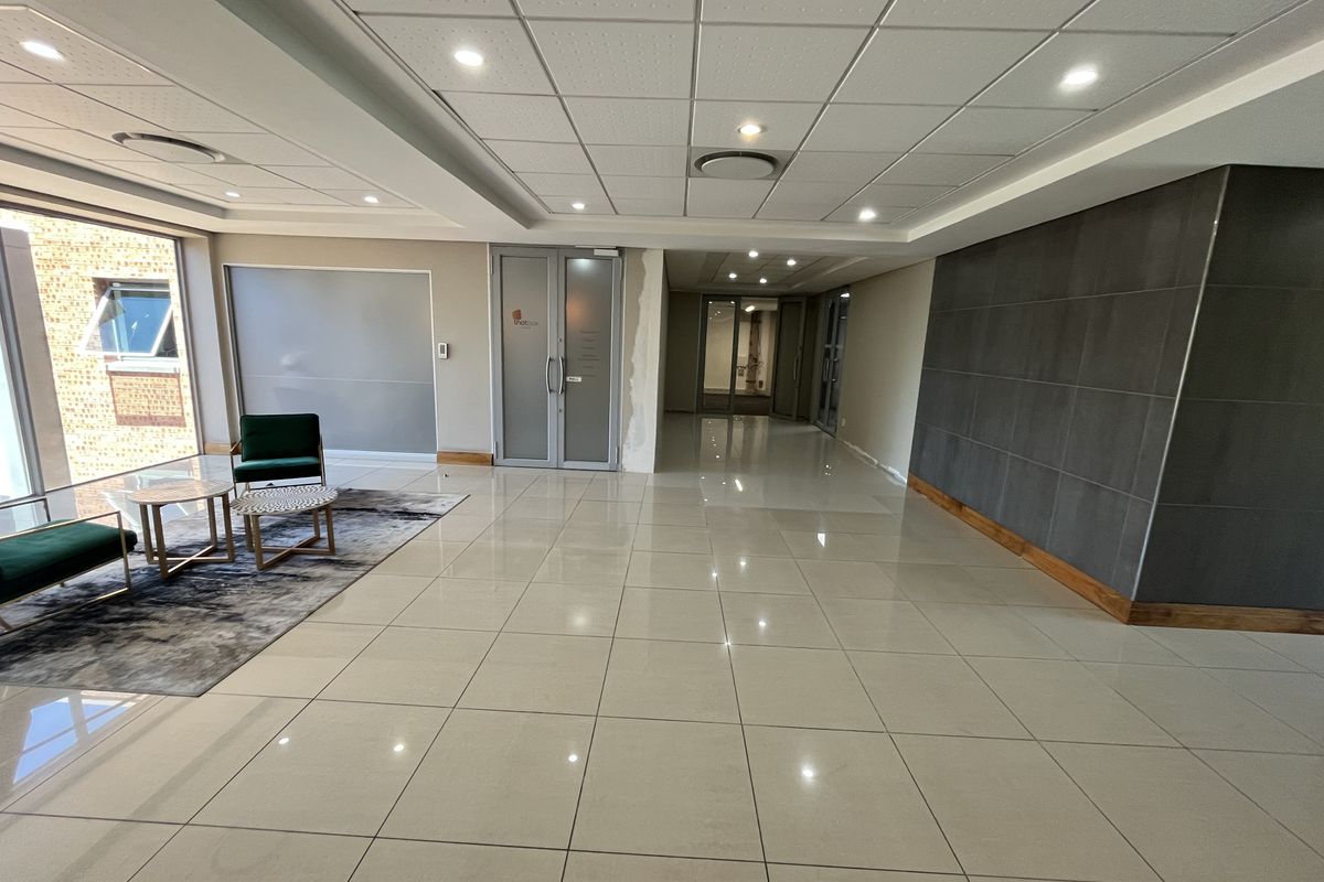 Modern office reception area featuring polished porcelain floor tiles, recessed lighting, suspended ceiling, and a contemporary tiled feature wall.