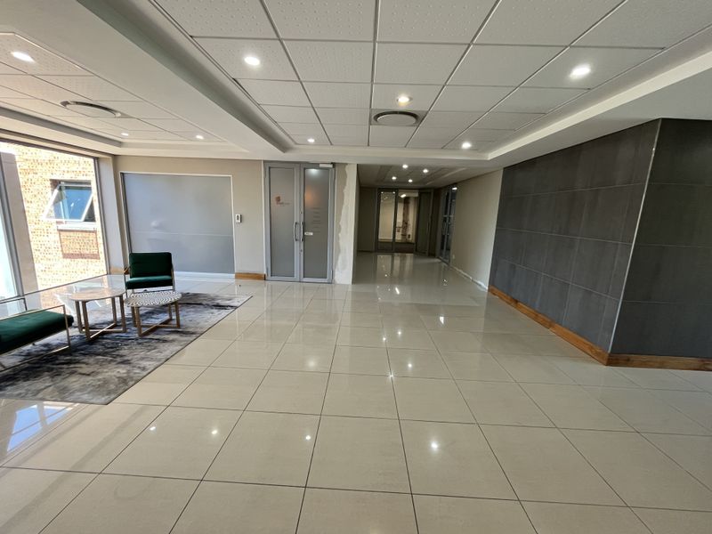 Modern office reception area featuring polished porcelain floor tiles, recessed lighting, suspended ceiling, and a contemporary tiled feature wall.