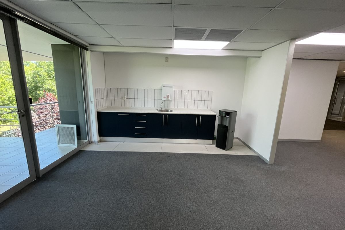 A clean, functional office kitchenette featuring built-in cabinetry, a sink, and direct access to an outdoor balcony area.