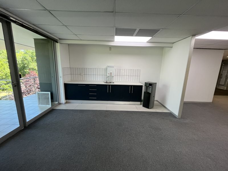 A clean, functional office kitchenette featuring built-in cabinetry, a sink, and direct access to an outdoor balcony area.