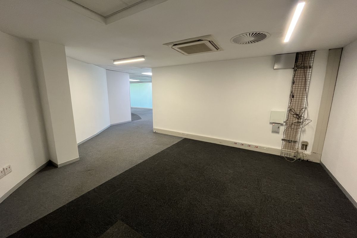 An empty office space featuring carpeted flooring, recessed ceiling lighting, integrated air conditioning, and visible wall-mounted electrical and data cabling.