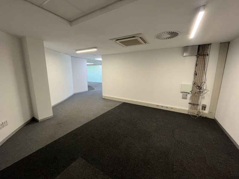 An empty office space featuring carpeted flooring, recessed ceiling lighting, integrated air conditioning, and visible wall-mounted electrical and data cabling.