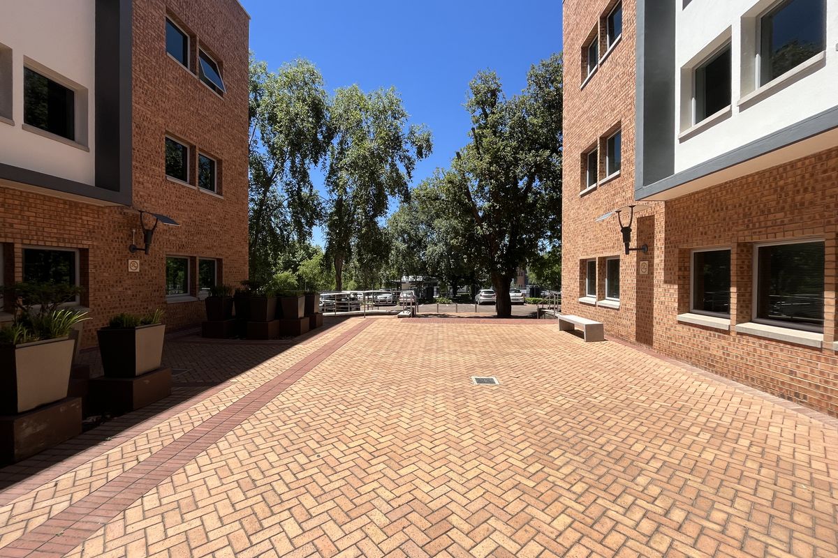 A well-maintained paved courtyard area situated between two modern brick office building wings, featuring clean lines and integrated exterior lighting.