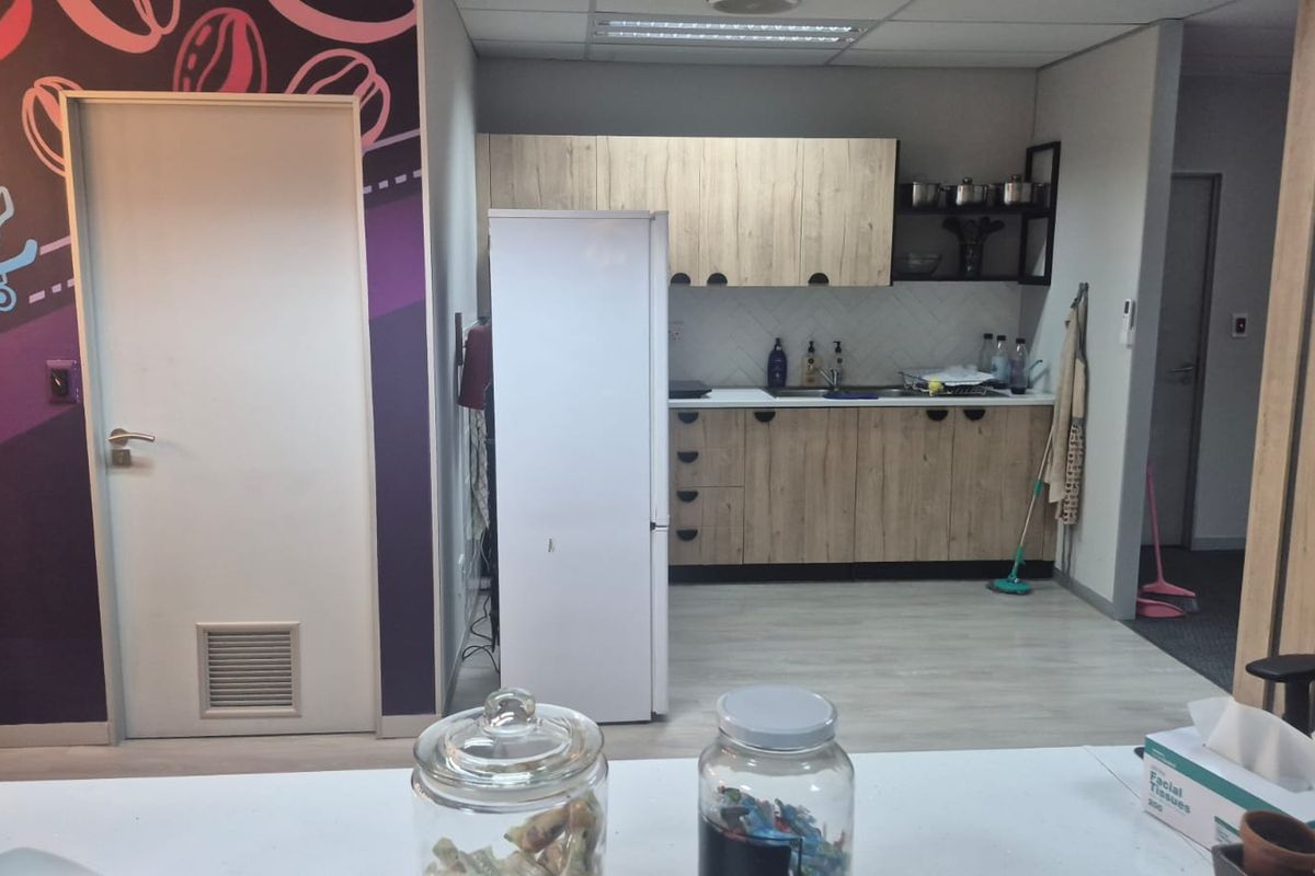 A functional office kitchenette featuring wood-look cabinetry, a tiled backsplash, and a stainless steel sink, providing a convenient break area for staff.
