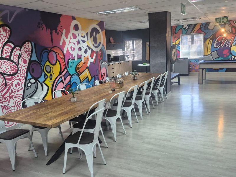 Spacious open-plan office breakout area featuring vibrant mural walls, laminate flooring, recessed lighting, and a functional kitchenette corner.