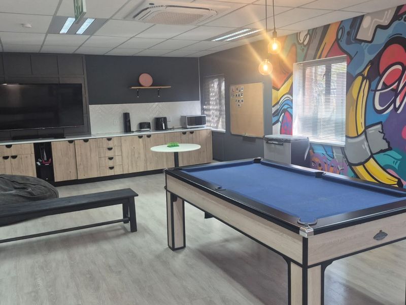 Modern office breakout area featuring built-in cabinetry, laminate flooring, recessed ceiling lighting, and air conditioning, designed for collaborative work and relaxation.