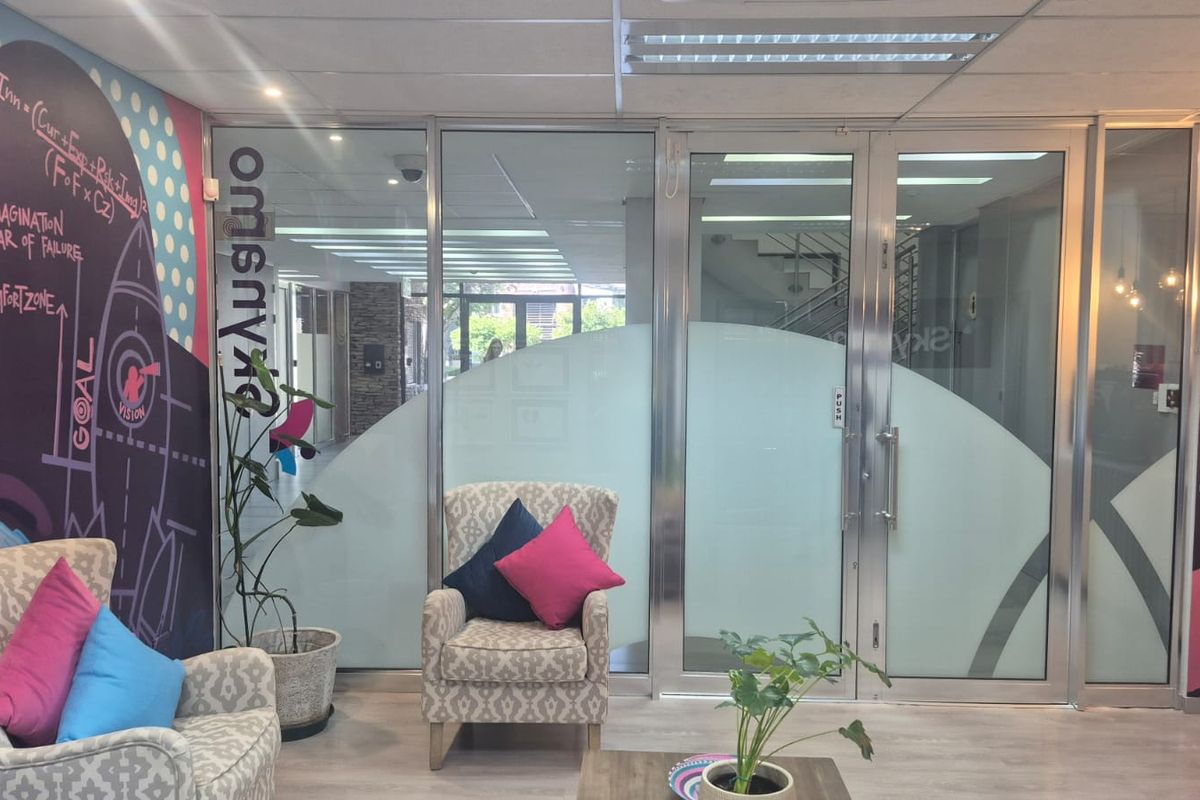 A modern office entrance area featuring a glass partition, aluminum-framed doors, and contemporary wall graphics.