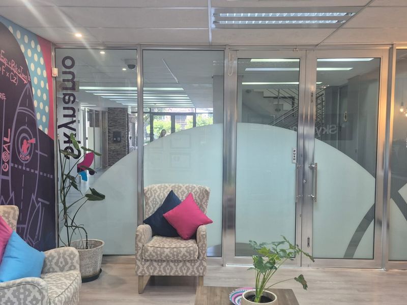 A modern office entrance area featuring a glass partition, aluminum-framed doors, and contemporary wall graphics.