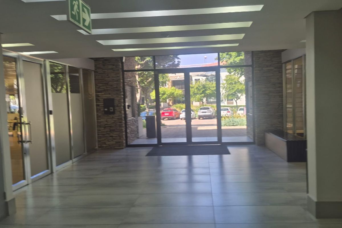 A bright and modern office building entrance lobby featuring stone-clad pillars, large glass doors, and clean tiled flooring.