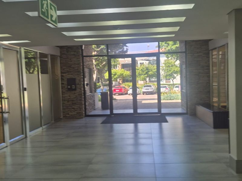 A bright and modern office building entrance lobby featuring stone-clad pillars, large glass doors, and clean tiled flooring.