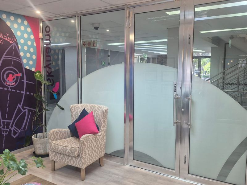 Modern office space featuring glass partitions, double glass doors, and a contemporary suspended ceiling with recessed lighting.
