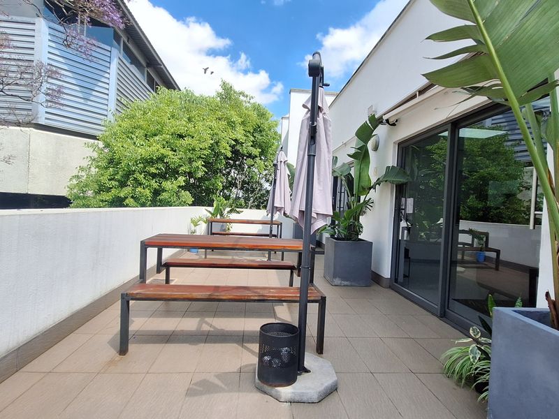 A well-maintained outdoor patio area featuring tiled flooring and sliding glass door access, suitable for office break-out space.