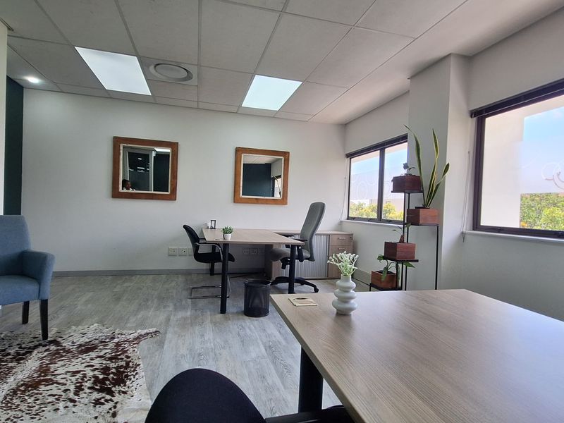 A bright and modern office space featuring large windows, suspended ceilings with recessed lighting, and durable laminate flooring.