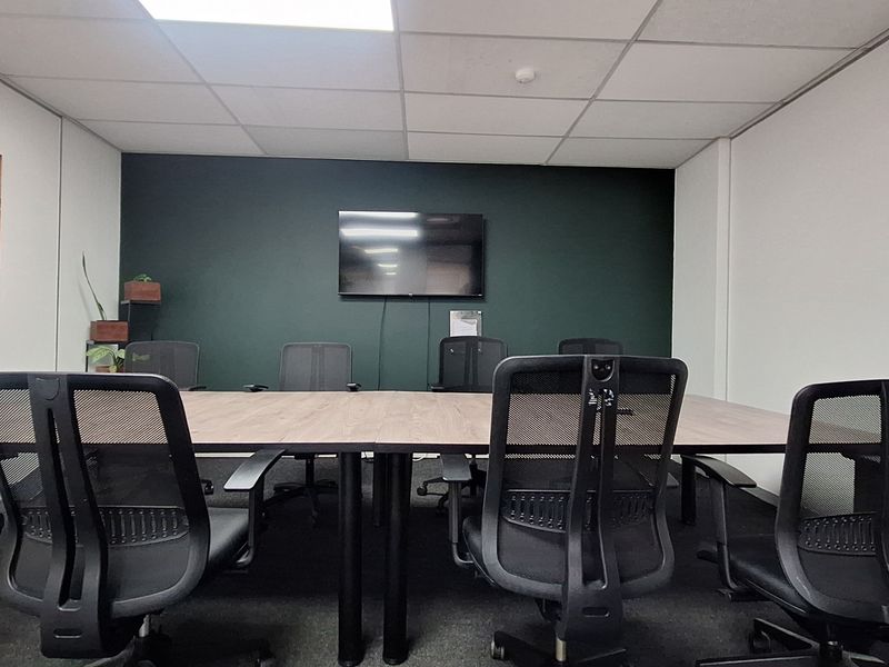 A professional office meeting room featuring a dark accent wall, suspended ceiling with recessed lighting, and a wall-mounted whiteboard.