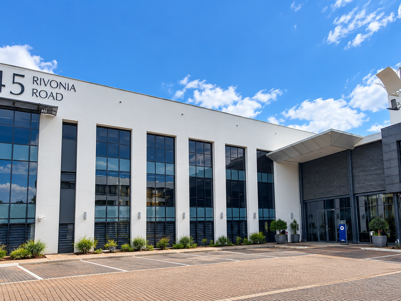 Modern commercial office building facade at 345 Rivonia Road, featuring extensive glass curtain walls, a paved parking area, and professional landscaping.