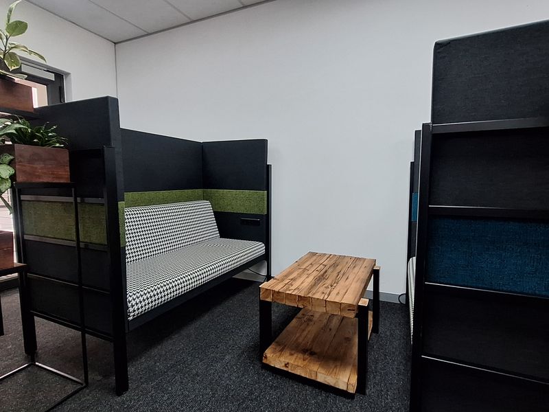 A modern office breakout area featuring carpeted flooring and a suspended ceiling, designed for collaborative work or casual meetings.