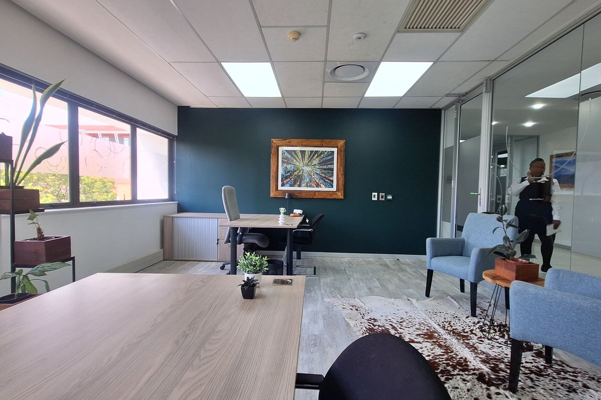 A modern office space featuring a dark accent wall, suspended ceiling with recessed lighting, and a glass partition wall, providing a professional work environment.