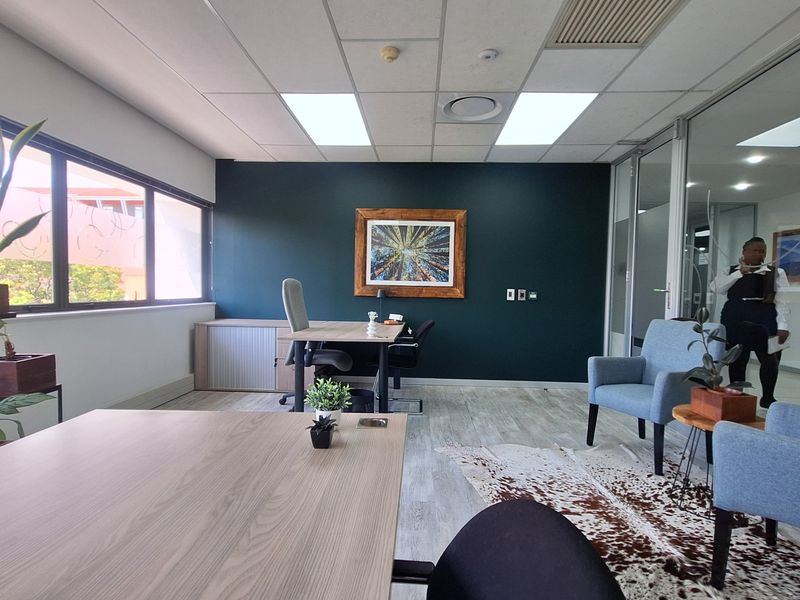 A modern office space featuring a dark accent wall, suspended ceiling with recessed lighting, and a glass partition wall, providing a professional work environment.