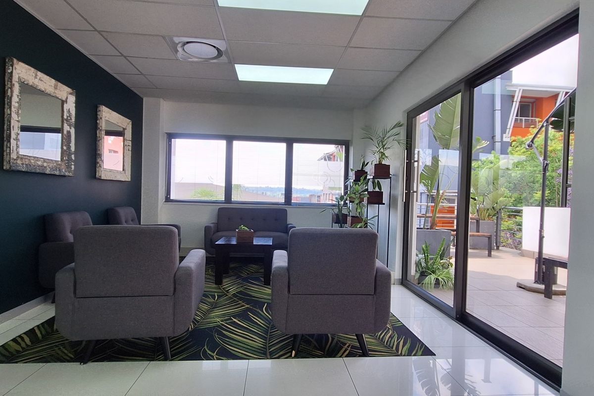 Modern office reception or waiting area featuring tiled floors, suspended ceiling, and large sliding glass doors leading to an outdoor balcony.