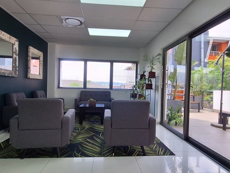 Modern office reception or waiting area featuring tiled floors, suspended ceiling, and large sliding glass doors leading to an outdoor balcony.
