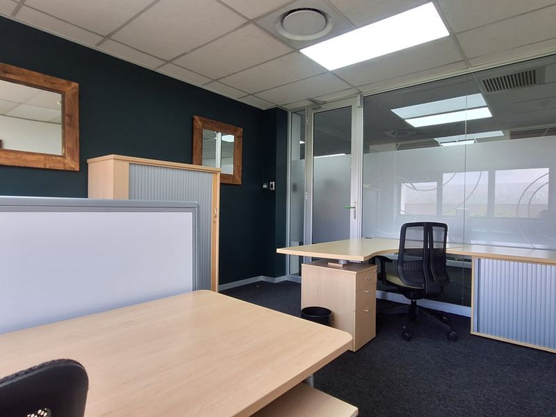 A professional office space featuring a glass partition wall, suspended ceiling with recessed lighting, and dark carpet flooring.